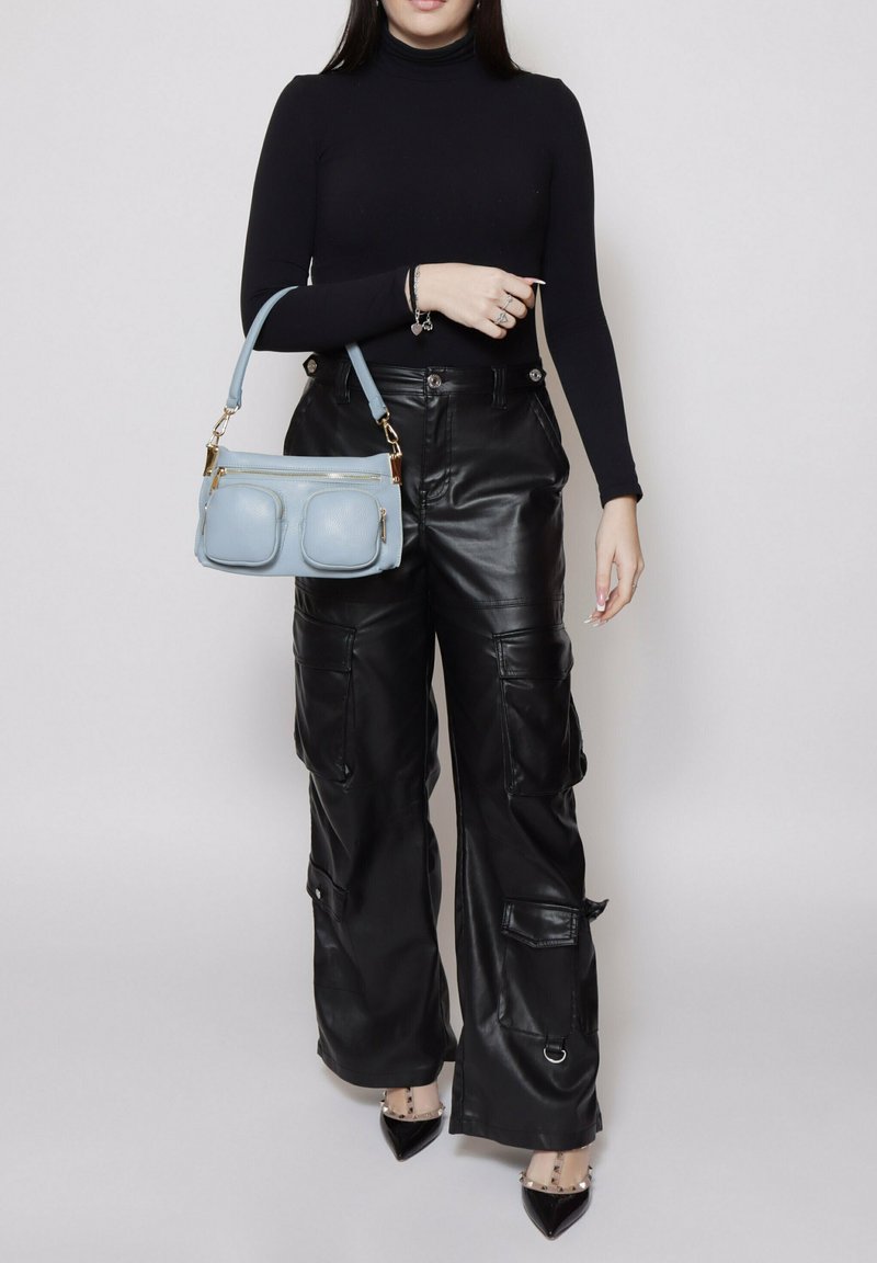 Pantaloni cargo in finta pelle nera con multiple tasche, abbinati a un dolcevita nero aderente e una borsa a tracolla azzurro chiaro con due tasche con zip.
