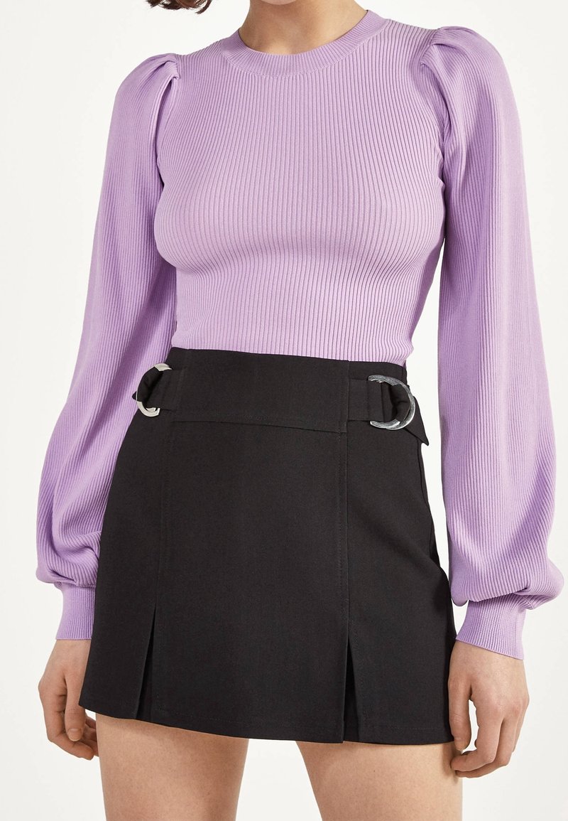 Maglia a maniche lunghe ribbata di colore viola chiaro abbinata a una gonna nera a vita alta con fibbie argentate e un design plissettato.