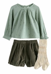 Blusa verde chiaro, con texture e ricami floreali, abbinata a pantaloni corti verdi scuri con vita elastica e calze sopra il ginocchio a coste color crema.