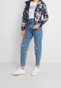 Laivaston kukallinen puffer-takki, vaaleanlila graafinen t-paita, kuluneet siniset farkut ja valkoiset alustakengät vaaleanpunaisilla pisteillä varustetuilla sukilla.