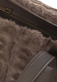 Borsa a mano marrone con interno in pelliccia sintetica soffice e esterno in pelle marrone. Presenta una chiusura con zip e una tracolla liscia. Dettagli di superficie testurizzata.