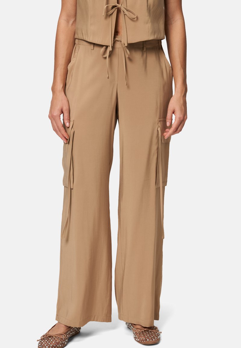 Beige wijde broekspijpen gemaakt van een gladde, lichte stof. Voorzien van twee zijvakken met flappen en een verstelbare tailleband met trekkoord.