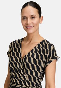 Robe portefeuille noire et beige avec un motif ondulé, décolleté en V, manches courtes et détail des épaules froncées. Tissu doux avec une texture lisse.