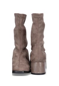 Botas de tobillo de ante marrón con un diseño holgado, que cuentan con un tacón bajo y costuras visibles a lo largo de las uniones. Textura suave en toda su superficie.