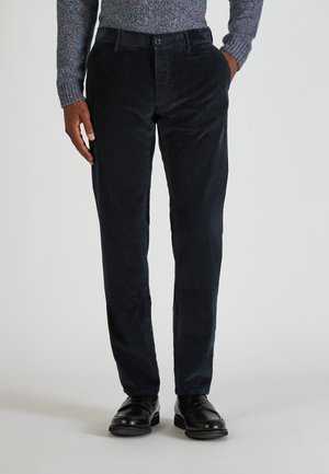 Marineblauwe corduroybroek met een slim fit, voorzien van een klassieke knoopsluiting en voorzakken. Gdragen met zwarte leren schoenen.