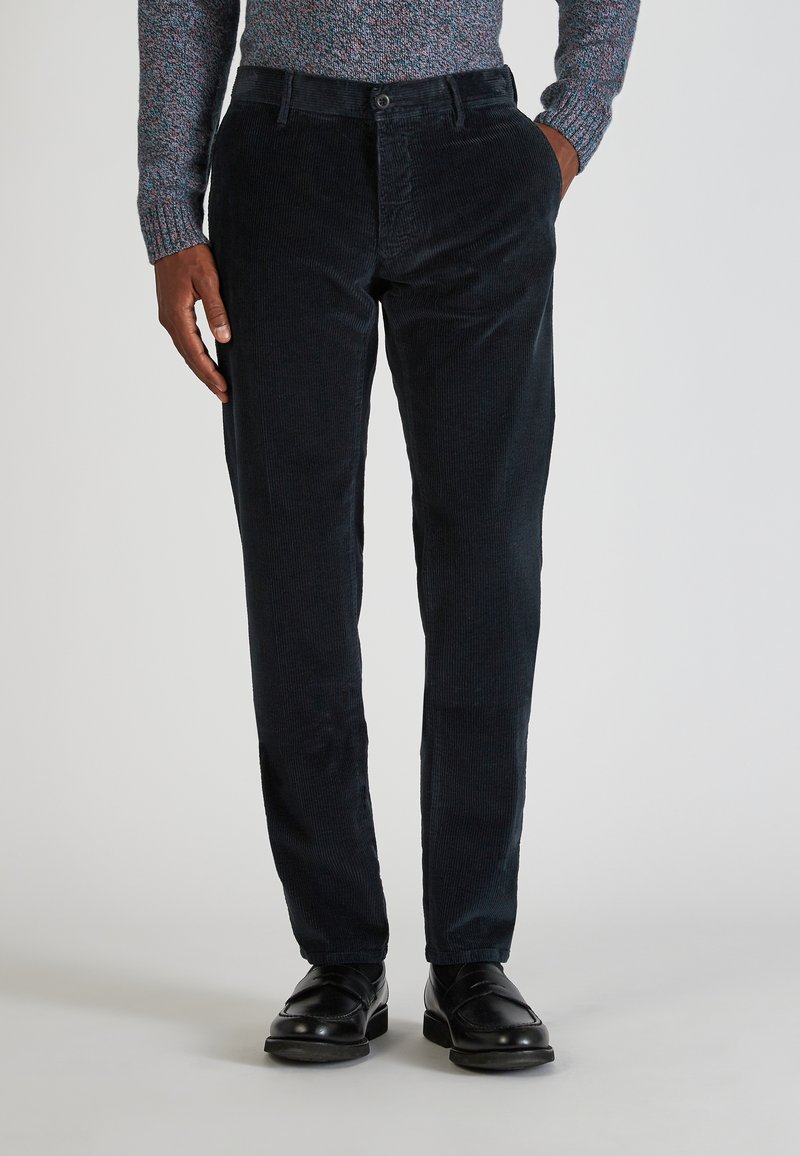 Granatowe spodnie kordowe o slim fit, z klasycznym zapięciem na guziki i kieszeniami z przodu. Noszone z czarnymi skórzanymi butami.