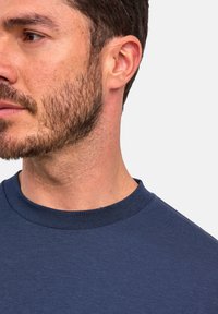 Navyblauwe katoenen T-shirt met ronde hals, met korte mouwen en een gladde textuur, gedeeltelijk zichtbaar op de schouder en hals van een persoon.