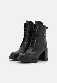Botines de cuero negro con tacón grueso, con cordones en la parte delantera, cuello acolchado, detalles metálicos y suela de goma texturizada.