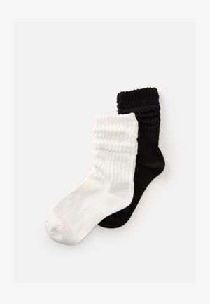 Deux chaussettes de ville côtelées, l'une noire et l'autre blanche, se chevauchent sur un fond blanc.