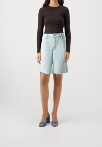 Světlé modré denimové šortky s roztrhanými okraji, kombinované s upnutým černým topem s dlouhým rukávem a modrými sandály na blokovém podpatku.