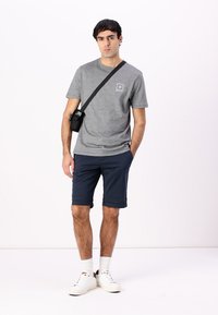 Grå bomulls T-skjorte med en liten logo, kombinert med marineblå shorts. Hvite sneakers og en svart crossbody-veske fullfører det uformelle utseendet.