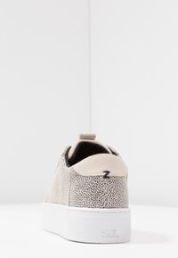 Baskets beiges à texture à pois, accents noirs et semelle épaisse blanche. Dotées d'une languette à l'arrière et d'un détail logo sur le côté.