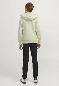 Sudadera verde claro con capucha ajustable, textura suave, puños y dobladillo acanalados, combinada con pantalones negros y zapatillas blancas.
