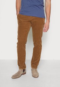 Hnědé kordové kalhoty s vertikálním žebrováním, slim fit design, přední kapsy, doplněné šedými semišovými kotníkovými botami.