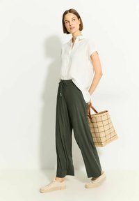 Biała koszula z krótkim rękawem z kołnierzykiem, ciemnozielone szerokie spodnie, beżowe sneakersy oraz torba z materiału w kratkę.