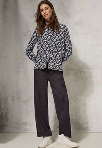 Langsleeve shirt in marineblauw met een wit ruitpatroon, gecombineerd met zwarte wijde broek en witte sneakers op een neutrale achtergrond.