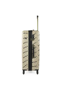 Maleta rígida en beige con patrón de logotipo negro de DKNY, cremallera negra y un mango retráctil dorado. Cuenta con cuatro ruedas para mayor movilidad.