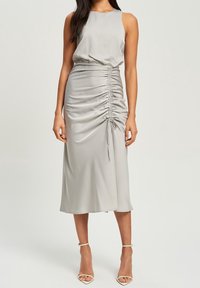 Ärmlös grå midiklänning i mjukt material, med rynkdetaljer längs kjolen och dragskoakenter vid midjan.