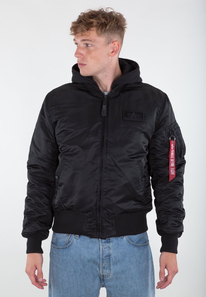 Black bomber jacket with a hood, made of shiny nylon. Features ribbed cuffs, waistband, and a red tag on the sleeve with text.