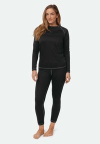 Zwarte thermische top met lange mouwen en nauwsluitende legging, gemaakt van een zacht materiaal met contrasterende stiksels. Het ontwerp is aansluitend en praktisch.
