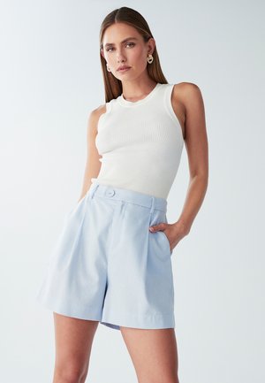 Lichtblauwe geplooide shorts met een knoopsluiting, gemaakt van geweven stof, gecombineerd met een aangesloten witte geribbelde tanktop.