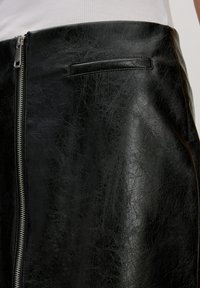 Zwarte leren rok met een gladde textuur, zichtbare ritsdetails aan de zijkant en een strakke, minimalistische uitstraling.