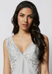 Sidenliknande grå camisole med djup V-halsringning, spetsdetaljer vid axlarna och blommig spetsdekoration på bysten.