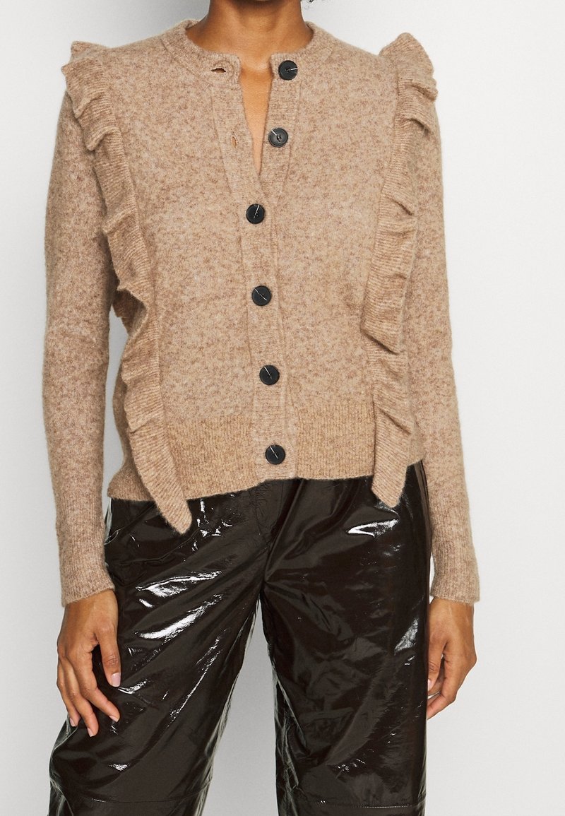 Cardigan beige en tricot avec une finition texturée, doté d'une rangée de boutons noirs et de détails froncés le long des épaules et des côtés.