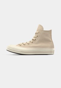 Høye sneakers i beige skinn med gummitupp, flate snøringer og kontrasterende hvit mellomsåle. Teksturert overflate med sømdetaljer.