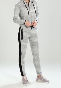 Grårandig hoodie med dragkedja i nacken, kombinerad med grå joggers som har svarta sidopaneler och logotyp. Bärs med grå sportskor.