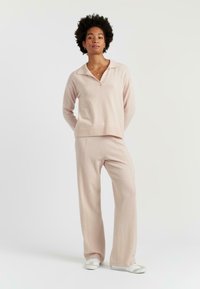 Lichtroze gebreide pullover met een V-hals en een geribde zoom, gecombineerd met bijpassende wijde broek met voornaad en witte sneakers.