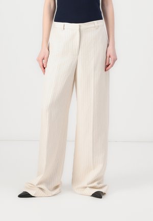 Pantalons larges couleur crème avec un motif de fines rayures, taille cintrée et chaussures noires à bout pointu.