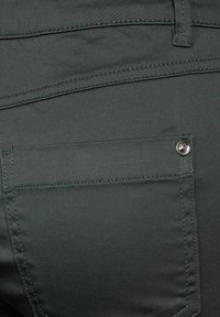 Pantalones de tela verdes que presentan un bolsillo trasero con un botón a presión de metal, costuras rectas y una textura suave.
