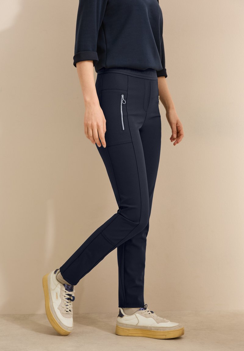 Navy blue stretch pants made of smooth fabric, featuring side zip pockets, a tapered silhouette, and an elastic waistband.
