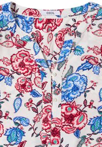 Blouse blanche à motif floral rouge et bleu, col rond, patte de boutonnage partielle et étiquette de marque "Cecil" à l’encolure.