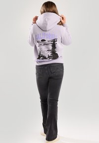 Fialová mikina s potiskem hor a stromů, se textem "NÁRODNÍ PARK KALIFORNIE" pod obrázkem. Kombinováno s černými rozšířenými džíny.