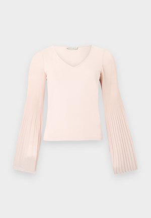 Haut rose clair à manches longues avec col en V et manches évasées plissées, présenté sur un fond gris clair uni.