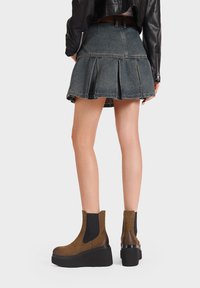 Stivali alla caviglia in suede marrone con pannelli elastici ai lati e una spessa suola nera, abbinati a una gonna plissettata in denim.