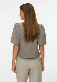 Siva bluza kratkih rukava s nabraniim rukavima i zaobljenim rubom, izrađena od teksturirane tkanine. Nošena s laganim bež hlačama.