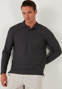 Polo de manga larga de color gris oscuro, elaborado en tejido texturizado, con cuello y tapeta de tres botones, con un corte relajado y detalles sutiles.