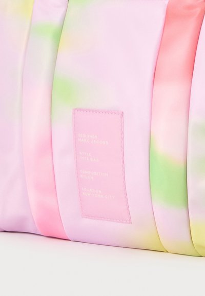 Sac fourre-tout tie-dye rose pastel, vert et jaune avec une étiquette rose indiquant le créateur et les détails sur le matériau. Aucun personne visible.