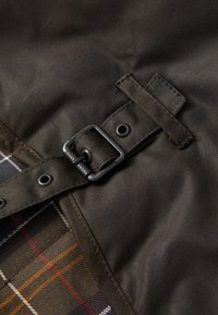 Close-up de um tecido escuro com uma fivela de metal preta e um forro de padrão tartan por baixo da costura.