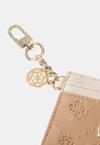 Portafoglio in pelle beige con design impresso. Hardware dorato che include una clip e una catena con un charm decorativo a forma di logo. Texture liscia.