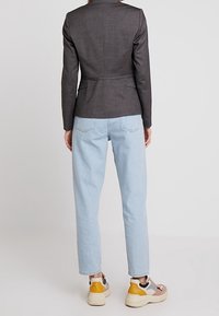 Blazer gris foncé ajusté avec une coupe structurée, associé à un jean droit bleu clair et des baskets multicolores.