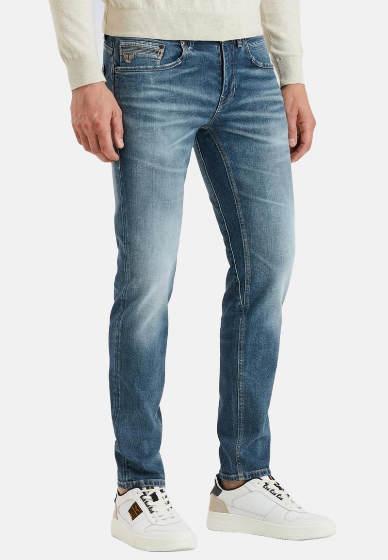 Jeans azules desgastados con un corte slim y detalles sutiles de arrugas, combinados con zapatillas blancas con acentos en negro y beige.