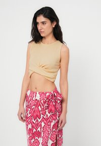Ριμπ υφής, ανοιχτό κίτρινο αμάνικο crop top με λεπτομέρεια στριφώματος, συνδυασμένο με ροζ και λευκή φούστα τύπου wrap με σχέδιο και δέσιμο στη μέση.