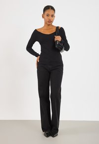 Svart ribbet langermet topp med vid utringning, kombinert med svarte rette jeans. Modellen holder en liten svart veske, og har på seg spisse høyhælte sko med nagler.