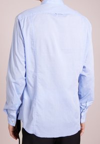 Lichtblauwe langearmige shirt met een button-down kraag, gemaakt van een gladde stof. Heeft een rechte achterkantnaad en knoopmanchetten.