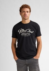T-shirt in cotone nero con testo stampato bianco che recita "Petrol Ind Speed Race Daytona 500", colletto rotondo, maniche corte e vestibilità rilassata.