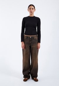 Černý top s dlouhým rukávem v kombinaci s volnými, vybledlými hnědými džíny. Oblečení doplňují hnědé ploché slip-on boty.